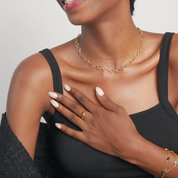 Woman wearing a black top and gold jewelry against a plain background