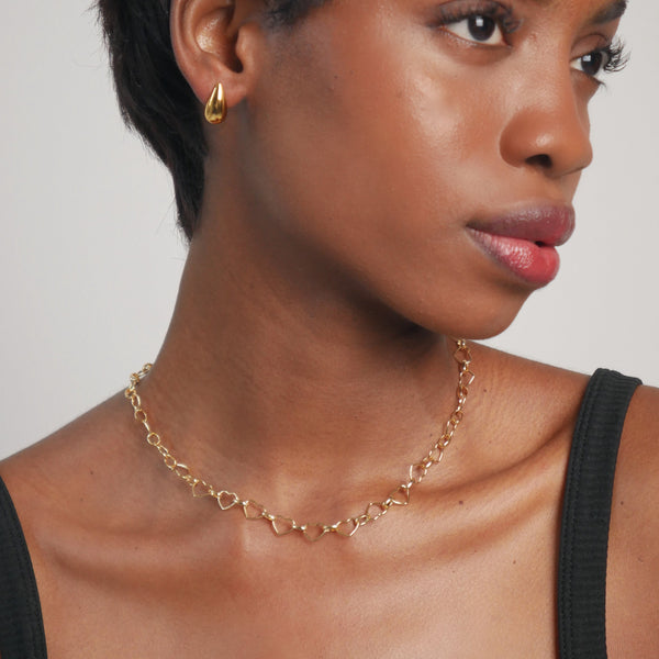 Woman wearing a gold necklace and earring against a neutral background